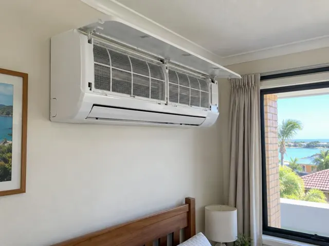 Open wall-mounted split system with clean filters above a bed in a bright bedroom in Runaway Bay