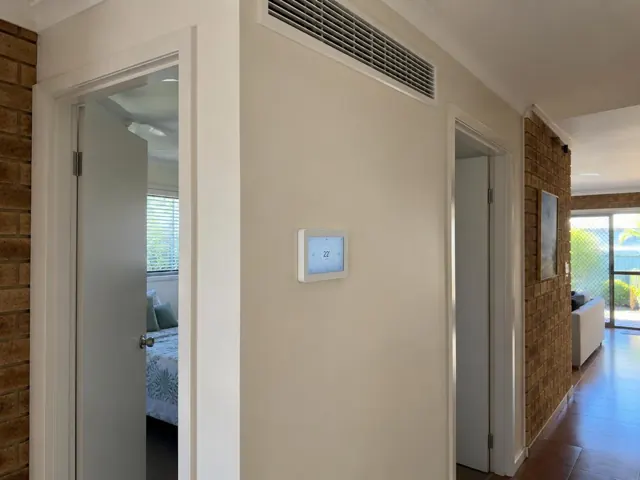Hallway wall controller and ceiling return-air grille in a brick home interior in Hope Island