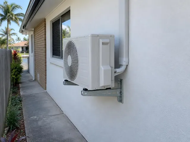Wall-mounted outdoor air conditioner unit beside a house exterior with a paved side path in Paradise Point