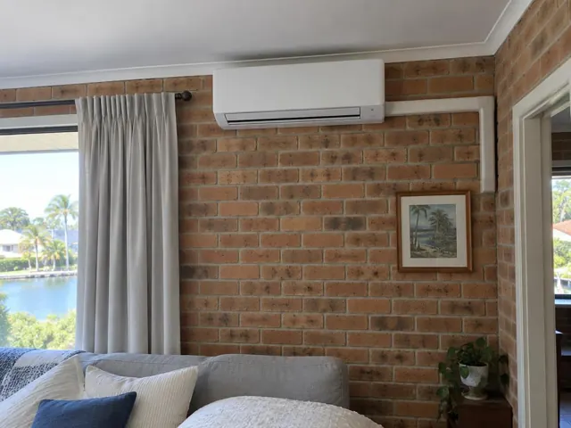Wall-mounted split system on a brick living room wall with curtains and window water view in Paradise Point